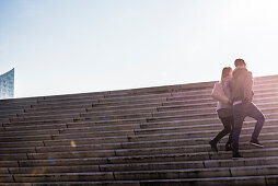 A young couple climbing up the steps of the new Elbe promenade with view of the Elbphilharmonie, Hamburg, Germany