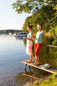 Two women drinking wine at the lakeshore, sunset, boats, lake Zethner See, summer, Mecklenburg lakes, Mecklenburg lake district, MR, Diemitz, Mecklenburg-West Pomerania, Germany, Europe