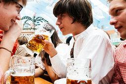 Young man in traditional cloth drinking beer in beer tent at Oktoberfest, Munich, Bavaria, Germany