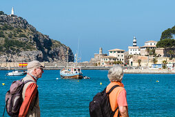 Wanderer auf der Promenade am Hafen mit Blick auf die zwei alten Leuchttürme, Port de Sóller, Mallorca, Spanien