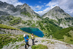 Man and woman hiking ascending towards Hinterer Tajakopf, lake Drachensee, Drachenkopf and Ehrwalder Sonnenspitze in background, Hinterer Tajakopf, Mieming Mountains, Tyrol, Austria