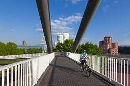 Radfahrerin auf einer Brücke über den Medienhafen, Blick zum Neuen Zollhof von Frank O. Gehry, Düsseldorf, Nordrhein-Westfalen, Deutschland