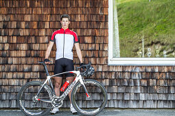 Young man standing at a wall next to his racing cycle at the Kitzbühler Alps, Kitzbühlerhorn, Tyrol, Austria