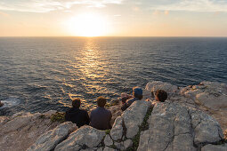 Vier junge Männer genießen den Sonnenuntergang auf einer Klippe am Strand Praia da Amoreira,  Aljezur, Faro, Portugal