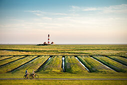 UNESCO World Heritage the Wadden Sea, cyclists passing Westerheversand lighthouse surrounded by salt meadows, Westerhever, Schleswig-Holstein, Germany, North Sea