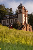 Man rides mountain bike through meadow in front of Gruftkapelle der Grafen von Ingelheim chapel, Mespelbrunn, Räuberland, Spessart-Mainland, Franconia, Bavaria, Germany