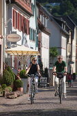 Couple ride bicycles along Main river promenade, Marktheidenfeld, Spessart-Mainland, Franconia, Bavaria, Germany