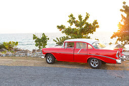 red oldtimer on a lonely coast road from La Boca to Playa Ancon, with beautiful small beaches in between,  turquoise blue sea, family travel to Cuba, parental leave, holiday, time-out, adventure, near Trinidad, Cuba, Caribbean island