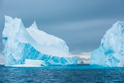 Ein Zodiac Schlauchboot und das Expeditions-Kreuzfahrtschiff MS Bremen (Hapag-Lloyd Cruises) wird von einem turmhohen Eisberg überragt, Active Sound, Antarktis