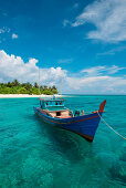 A colorful boat drifts in clear turquoise water off an island, Senua Island, Riau Archipelago, Indonesia, Asia