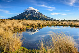 Vulkan Mount Egmont spiegelt sich in See, Person steht im Hintergrund, Egmont Nationalpark, Taranaki, Nordinsel, Neuseeland