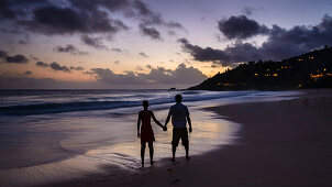Ein verliebtes Päärchen Hand in Hand bei Sonnenuntergang am Intendance Beach, Mahé, Seychellen