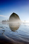 USA, Oregon, Pacific City, individuals walk along Pacific City Beach with Haystack Rock in the distance