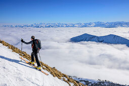 Man backcountry skiing ascending towards Hinteres Sonnwendjoch, fog in the valley, Hinteres Sonnwendjoch, Bavarian Alps, Tirol, Austria