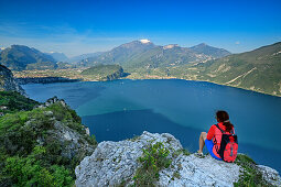 Woman hiking sitting at rock and looking towards lake Garda and Garda Mountains, lake Garda, Garda Mountains, Trentino, Italy