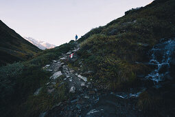 Hiker on long distance hiking path with mountain stream in the foreground, E5, Alpenüberquerung, 6th stage, Vent,Niederjochbach, Similaun hut, Schnalstal, Vernagt reservoir, Meran