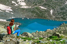 Frau beim Bergsteigen sitzt vor herzförmigem See Lago Chiaretto, Giro di Monviso, Monte Viso, Monviso, Cottische Alpen, Piemont, Italien