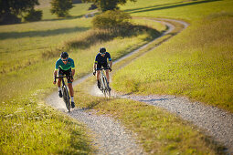 Zwei junge Männer fahren auf Gravel bikes über Feldweg, Münsing, Bayern, Deutschland