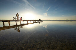 Young  woman and young man with bicycles on a jetty, Muensing, bavaria, germany