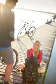 junge Frau  und junger Mann mit Fahrrädern auf Steg am Seeufer , Starnberger See, Bayern, Deutschland