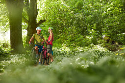 junge Frau und junger Mann Paar auf Fahrradtour in Waldstück mit Bärlauch, Kochel, Bayern, Deutschland