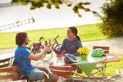 junge Frau und junger Mann  auf Fahrradtour,machen Pause im Biergarten, Münsing, Starnberger See, Bayern, Deutschland