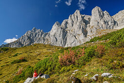 Woman hiking sitting on rock and looking towards rock walls of Kaiser, Wilder Kaiser, Kaiser range, Tyrol, Austria