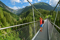 Frau steht auf Hängebrücke und blickt in die Tiefe, Holzgau, Lechweg, Lechtal, Tirol, Österreich