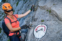 Frau am Klettersteig deutet auf Symbol Schlüsselstelle, Absamer Klettersteig, Bettelwurf, Karwendel, Tirol, Österreich
