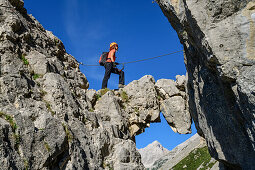 Frau steigt über Felsbogen am Klettersteig zum Bettelwurf auf, Absamer Klettersteig, Bettelwurf, Karwendel, Tirol, Österreich