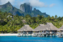 Overwater bungalows on stilts from a luxury resort are dwarfed by the high mountains in the background, Bora Bora, Society Islands, French Polynesia, South Pacific