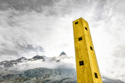 Gelber Origenturm ragt in den Himmel mit Bergen im Hintergrund, Julierpass, Graubünden, Schweiz, Europa