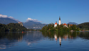 Wallfahrtskirche Mariä Himmelfahrt auf Insel im Bleder See mit blauem Himmel und Spiegelung, Bled Slowenien\n