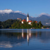 Wallfahrtskirche Mariä Himmelfahrt auf Insel im Bleder See mit blauem Himmel und Spiegelung, Bled, Slowenien