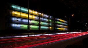 Colorfully lit apartment building with car lights at night, Munich