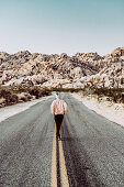 Frau läuft auf Straße im Joshua Tree National Park, Los Angeles, Kalifornien, USA, Nordamerika