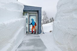 Woman enters the entrance area of a modern mountain hut, Seethalerhütte, Dachstein, Upper Austria, Austria through a snow tunnel