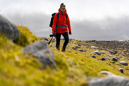 Fotografin wandert durch die grasbewachsene Berglandschaft zwischen Saksun und Tjørnuvík, Streymoy, Färöer Inseln