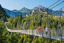 Several people walk over the Highline 179 rope bridge with Ehrenberg castle ruins in the background, Reutte, Tyrol, Austria