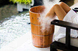 A woman having a footbath, in wooden barrel , with steam billowing. Horizontal. Kuala Lumpur, Malaysia.