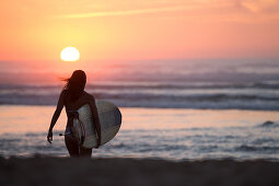 Surferin geht mit Surfbrett am Strand im Sonnenuntergang,  Portugal