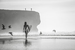 Female surfer walks on the beach in Portugal with her surfboard, surfing, Portugal