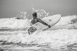 Surferin geht durch Wellen ins Wasser, Portugal