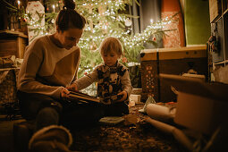 little boy with his mother looking at book in front of the Christmas tree, Christmas, family