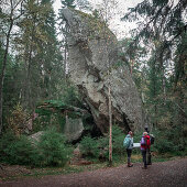 Wandergruppe steht vor großem stehenden Felsbrocken im Wald im Tiveden Nationalpark in Schweden\n