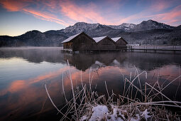 Holzhütten und Steg am Kochelsee bei Sonnenaufgang, im Vordergrund das vereiste Seeufer, Schlehdorf, Bayern, Deutschland, Europa