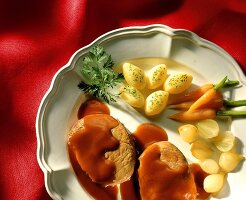 Roast pork with gravy and vegetables on white plate