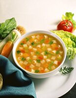 Gemüsebrühe mit Nudeln, daneben verschiedene Suppengemüse