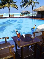 Two cocktails on a wooden table next to a pool with a view of the sea