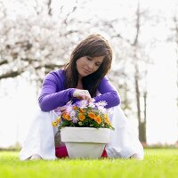 Frau auf Wiese bei Blumentopf mit Anemonen und Stiefmütterchen